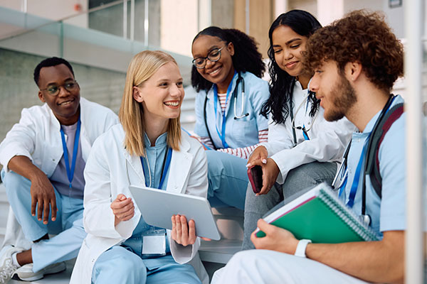 Four nursing students and a faculty member sit together, smiling and reviewing notes on a tablet.