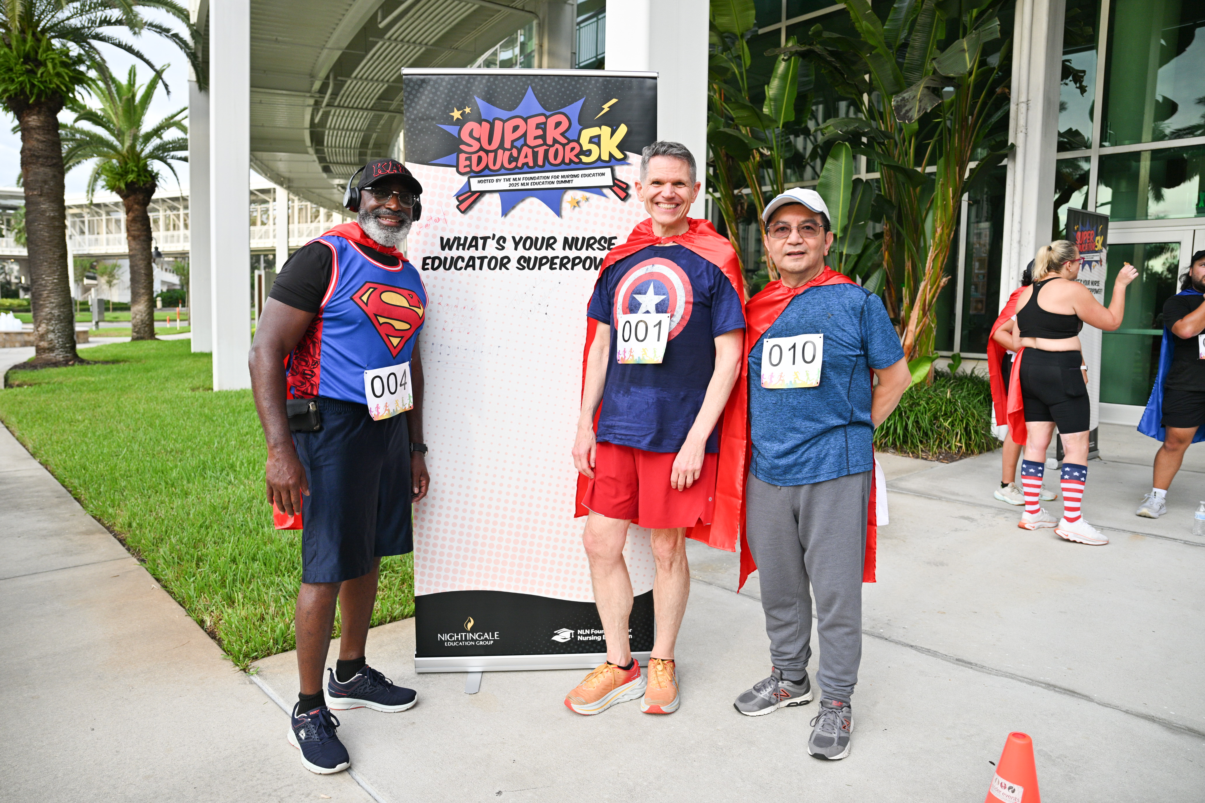 Three men stand in superhero-themed running attire by a signed poster.