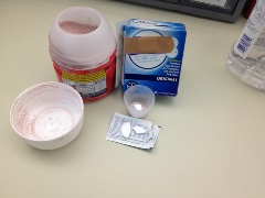 container of red powdered drink mix, box of adhesive bandages, effervescent antacid tablet broken into one quarter piece, and small plastic med cup