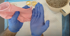 Hands in blue gloves hold a pink glove open on top of an absorbent pad. Nearby are two laundry pods and a container filled with cat litter.
