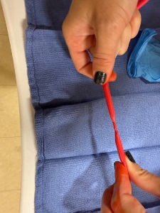 Two hands twist a red tube over a blue medical pad, with a blue glove lying nearby.