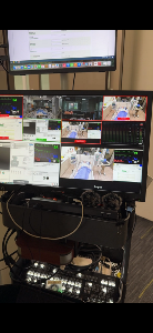 Equipment cart with lower monitor showing ATEM Mini Extreme multiview. Below are wireless microphones, voice changer, Mac mini M1, ATEM Mini Extreme, and cables neatly arranged.