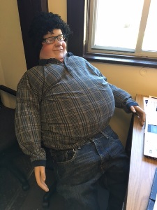 manikin with  a caricature obese mask wearing an obesity suit sitting in a desk chair