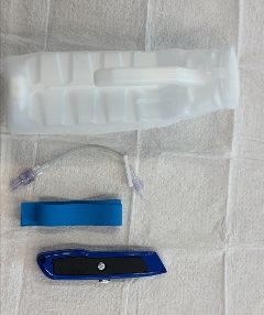A clear plastic bottle, a short IV extension tube, a blue tourniquet, and a blue utility knife are laid out on a white medical pad.