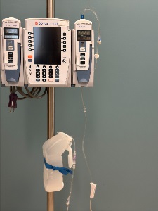 IV pump setup on a pole with two BD Alaris modules, connected tubing, and an empty plastic jug secured with a blue tie serving as a drainage container.