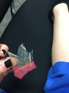 hand holding shard of glass with simulated blood on jagged edge