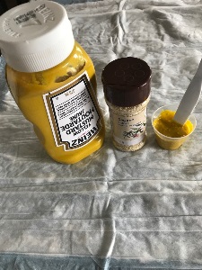 bottle of yellow mustard, container of sesame seeds, and a medication cup with yellow mustard and sesame seeds