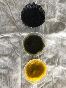 Three medication cups. One medication cup contains black substance. One medication cup contains dark green substance. One medication cup contains chunk yellow substance.