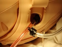 left side of manikin with tubing exposed only where it connects to the bleeding port and where it exits the manikin as the "chest tube"