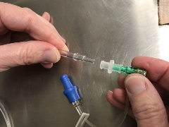 hands inserting the distal end of IV tubing into the other side of the female-to-female luer connector