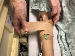 person attaching an elastic bandage to manikin forearm to conceal the drainable tubing