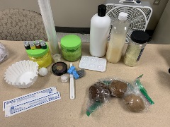 A collection of wound simulation materials on a table, including bottles of liquid, pigment containers, sponges, three reclosable plastic bags containing simulated skin clay, and medical supplies