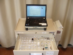 beige medical cart with top drawer open showing medications and a laptop on top of the cart