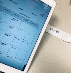 partial view of a tablet with eMAR on the screen and a patient ID band with QR code