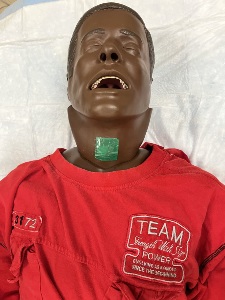 manikin with a covered tracheostomy shown from the chest up on a disposable underpad