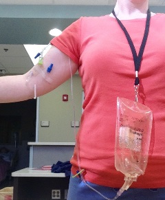 Standardized participant wearing a lanyard with IV fluid bag attached. Fluid bag has tubing attached to the standardized participant's upper arm.