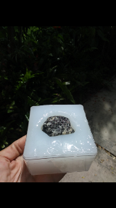 square container filled with silicone caulk with a rock placed on top of the silicone