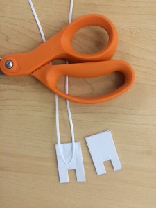orange scissor handle with plastic lacing and two 1.5” x 1” rectangles from adhesive craft foam with notch out of one end of each rectangle to simulate a plug
