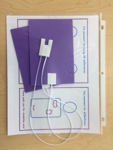 two purple simulated pads with simulated wiring on top of letter size paper with visual aid directing placement of pads heavyweight plastic sheet protector