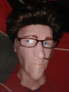 Halloween mask with brown hair wig, glasses, and ng tube threaded through nose
