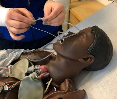 person threading string through bottom two holes of salem sump/NG tube after inserting the salem sump/NG tube in manikin's nose and pulling it out through mouth
