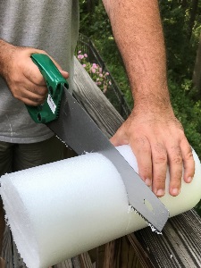 man using a hand saw to cut a high-density foam roller
