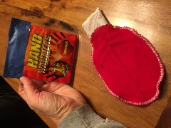 red fabric pocket with a disposable hand warmer being placed inside the pocket